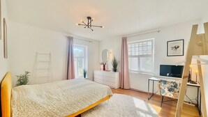 Ein Schlafzimmer mit einem Bett, einem Schreibtisch, einem Stuhl, einem Spiegel, einem Fenster und einer Deckenleuchte.