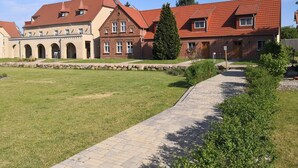 Ein Innenhof mit gepflastertem Weg, einem Backsteinhaus mit rotem Dach und einer Steinmauer.