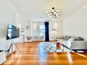A modern living room with a flat-screen TV, a grey sofa, a coffee table, and a chandelier.