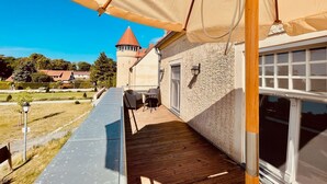 Ein überdachter Außenbereich mit Tisch und Stühlen, ein Gebäude mit Fenster sowie ein Turm im Hintergrund.