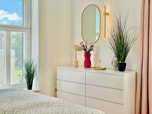 A bedroom with a bed, a dresser with drawers, a mirror, a lamp, and two potted plants.