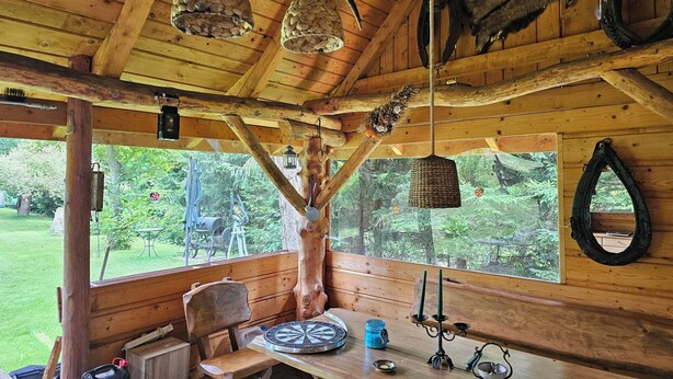 A rustic wooden cabin with a dining table, benches, and a view of the forest.