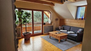 A cozy living room with a wooden floor, a sofa, a coffee table, and a large window with a view of trees.