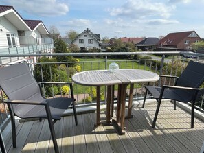 A wooden deck with a table and two chairs, overlooking a garden and neighboring houses.