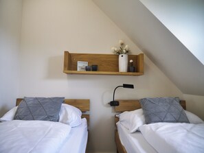 A bedroom with two beds, a wooden shelf above, and a nightstand with a lamp. - Küstenbude, 3 room apartment with balcony for 4 pers. (Büsum)