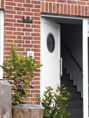 A brick building with a white door and a staircase leading inside. - Küstenbude, 3 room apartment with balcony for 4 pers. (Büsum)