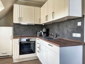 A kitchen with white cabinets, a Bosch oven, a coffee maker, and a modern faucet. - Küstenbude, 3 room apartment with balcony for 4 pers. (Büsum)