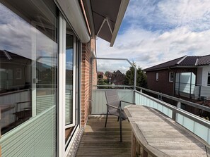 A balcony with a wooden floor, a chair, and a glass door leading to a room.
