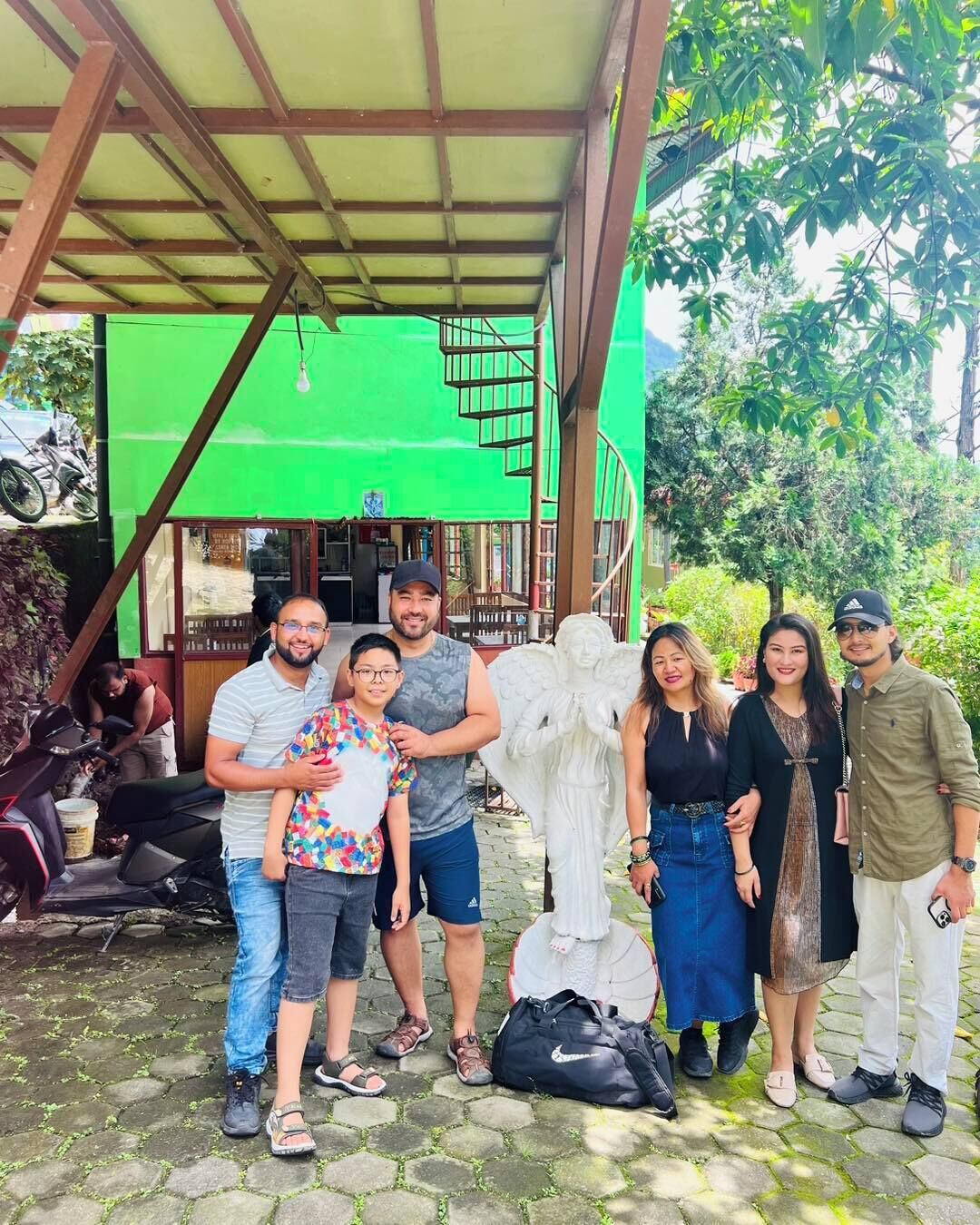 A group of people standing in front of a building with a green screen, a statue, and a motorcycle parked nearby.