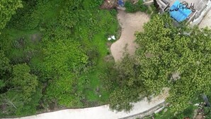 An aerial view of a residential area with multiple red-roofed houses, a paved road, and a small body of water. - Treez Resort Pvt Ltd (Burhanilkantha)