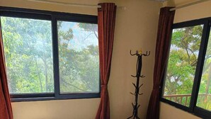A room with a bed, a bench, a coat rack, and a window with curtains. - Treez Resort Pvt Ltd (Burhanilkantha)
