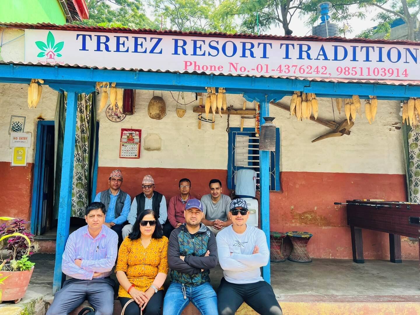 A group of people seated in front of a building with a sign reading "TREEZ RESORT TRADITION".