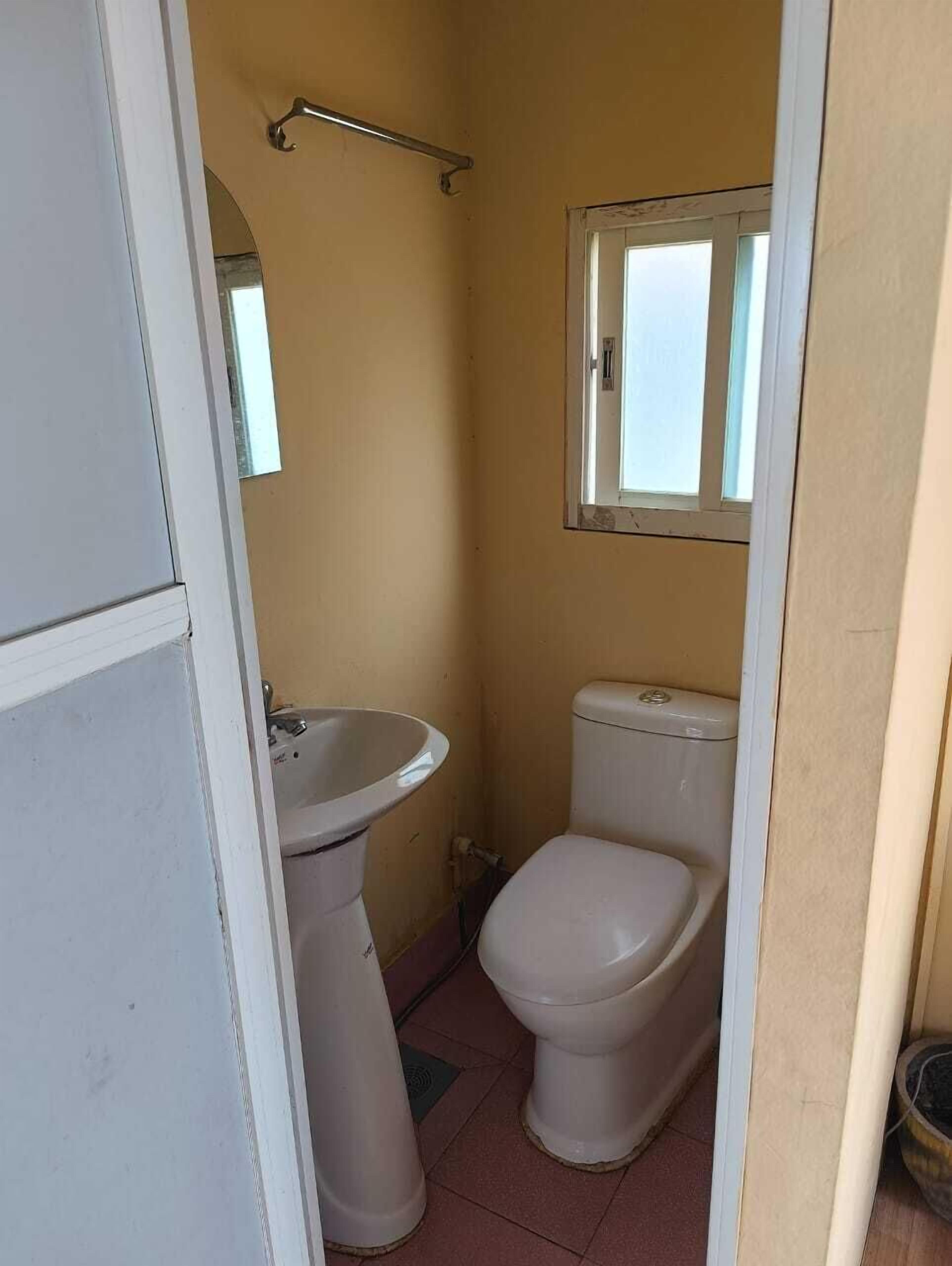 Un baño pequeño y estrecho con inodoro, lavabo y una ventana sobre el inodoro.