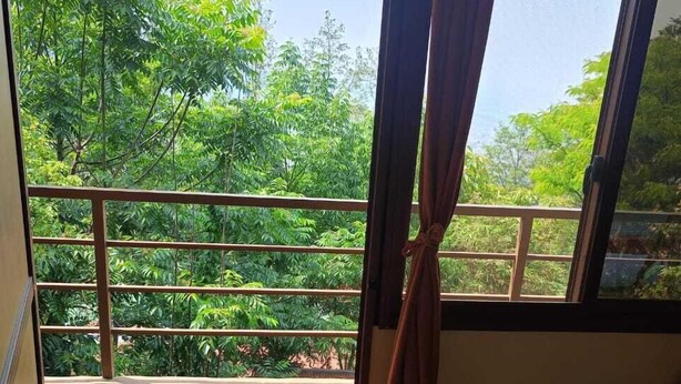 A room with a view of lush greenery through a window with curtains. - Treez Resort Pvt Ltd (Burhanilkantha)