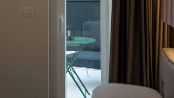 Quarto de hotel com cama, porta para uma varanda ao ar livre com mesa e cadeiras, e cortinas.