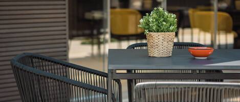 Un espacio de estar al aire libre con sillas de metal y una mesa, una cesta tejida con una planta y un cuenco.