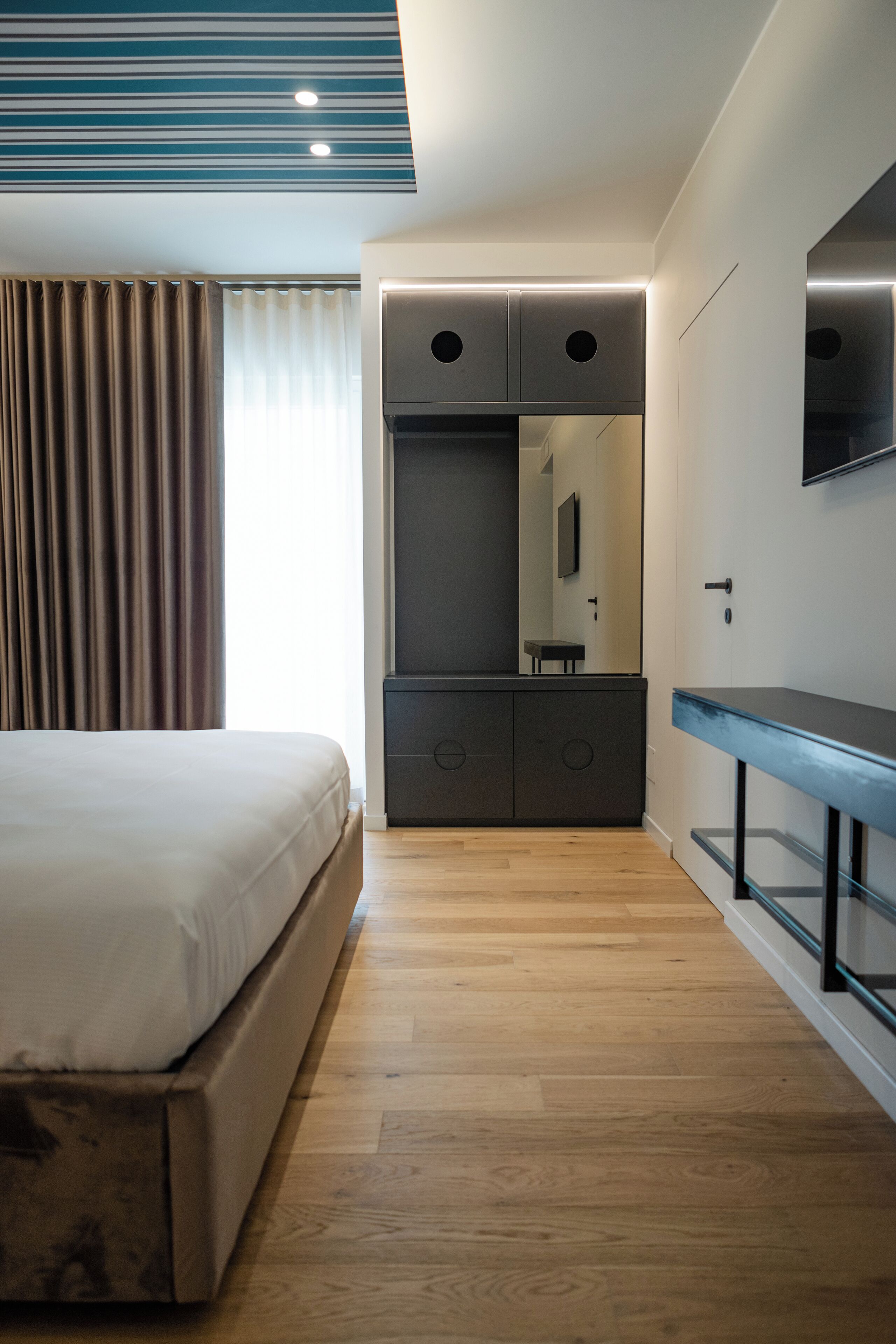 A modern hotel room with a large bed, a built-in wardrobe, a mirror, and a flat-screen TV.