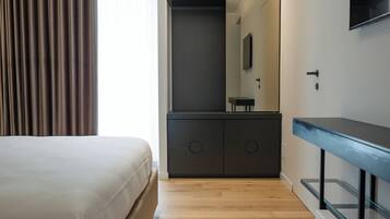 A modern hotel room with a large bed, a built-in wardrobe, a mirror, and a flat-screen TV.