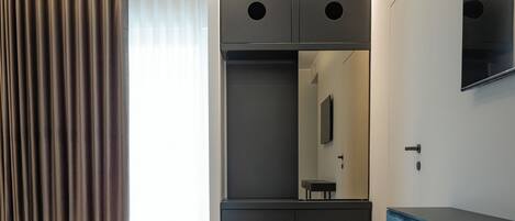 A modern hotel room with a large bed, a built-in wardrobe, a mirror, and a flat-screen TV.