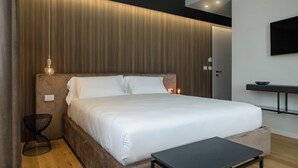 Ein modernes Schlafzimmer mit einem großen Bett, einem Nachttisch, einem wandmontierten Fernseher und einer eingebauten Ablagefläche.