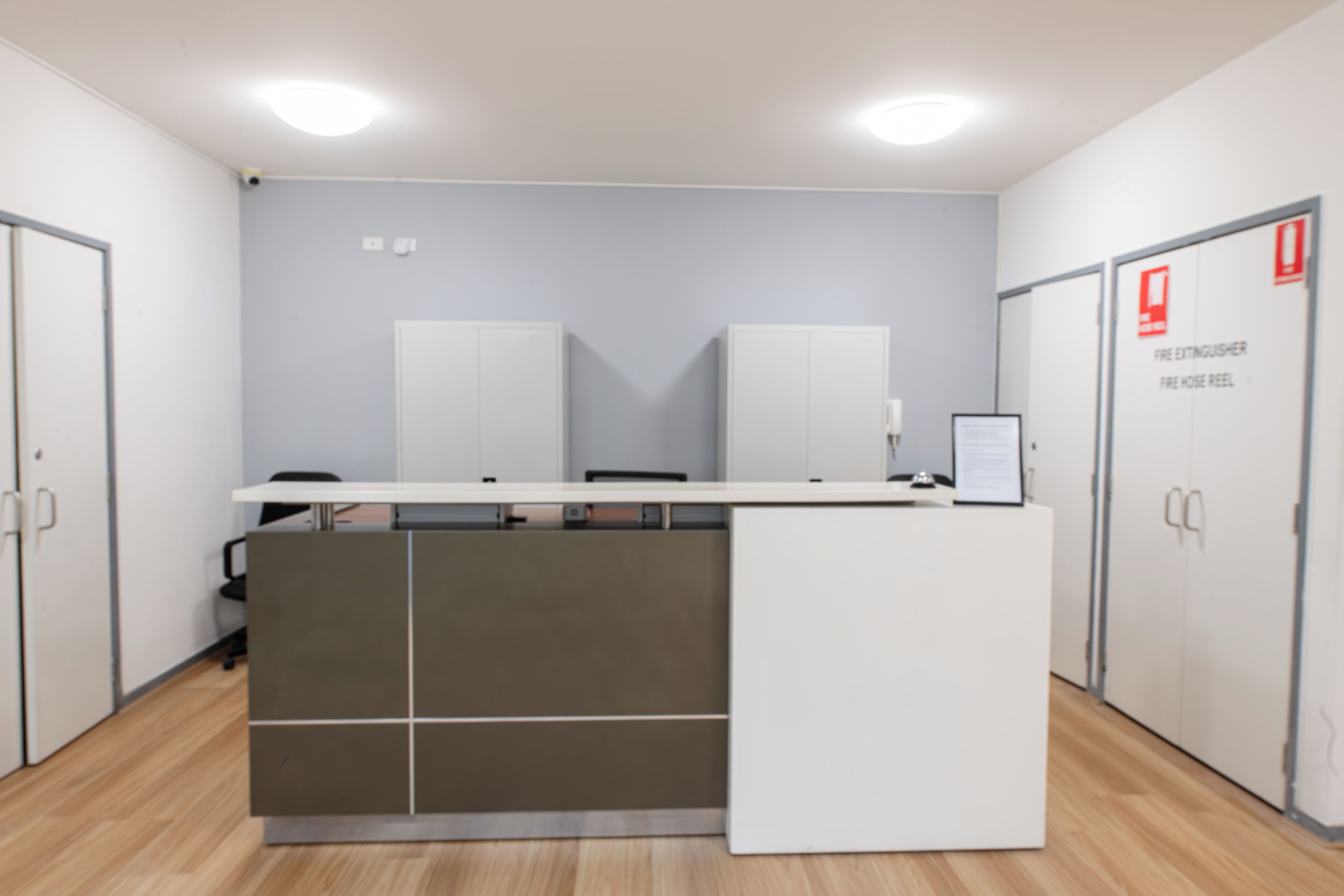 Un espacio de oficina moderno con un mostrador de recepción, dos armarios blancos y un armario para extintor.