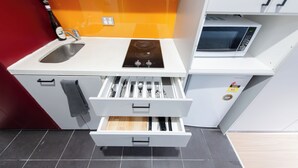 A compact kitchen with a sink, stove, microwave, and a drawer with utensils. - Melbourne Studio Apartments Hotel @ 138 Elgin Carlton (Carlton)