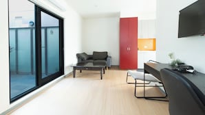 A modern living room with a sofa, coffee table, and a dining area with a table and chairs. There is a red cabinet and a TV mounted on the wall. - Melbourne Studio Apartments Hotel @ 138 Elgin Carlton (Carlton)