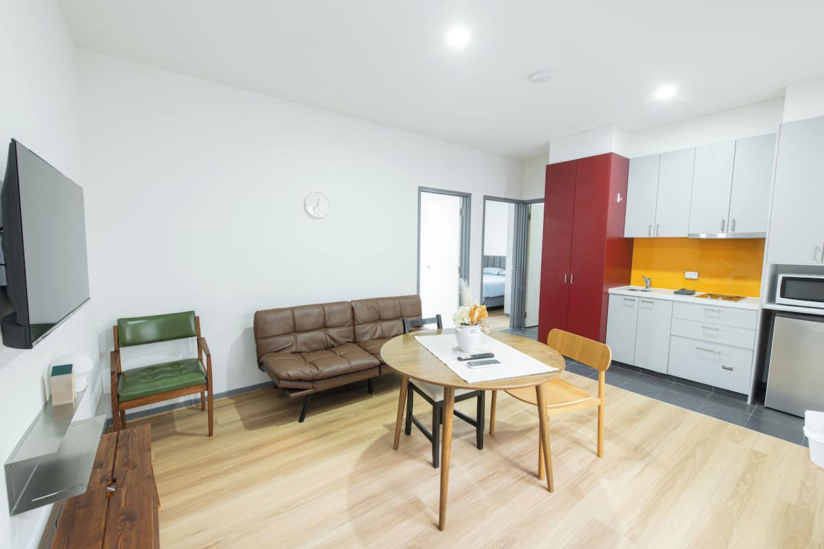 A modern living room with a brown leather sofa, a wooden dining table, and a TV mounted on the wall.