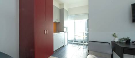 A modern kitchen with a red wardrobe, a dining area with a grey chair, and a small table.