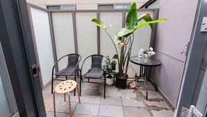 A small outdoor seating area with two wicker chairs, a small round table, and a potted plant. - Melbourne Studio Apartments Hotel @ 138 Elgin Carlton (Carlton)