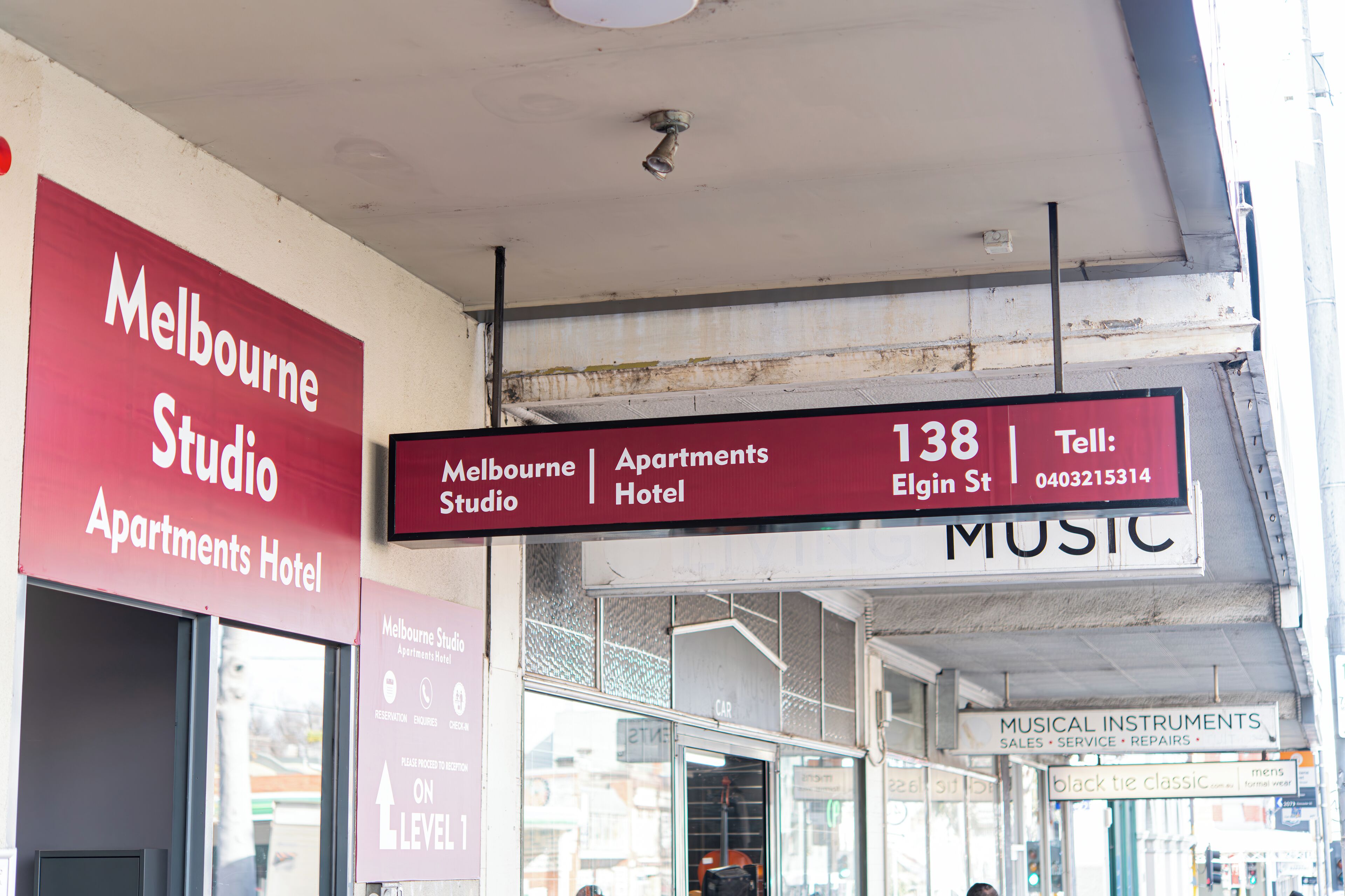 A signboard for the Melbourne Studio Apartments Hotel with contact information and a directional arrow indicating the location.