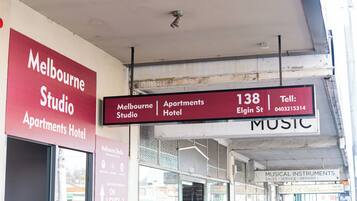 A signboard for the Melbourne Studio Apartments Hotel with contact information and a directional arrow indicating the location.