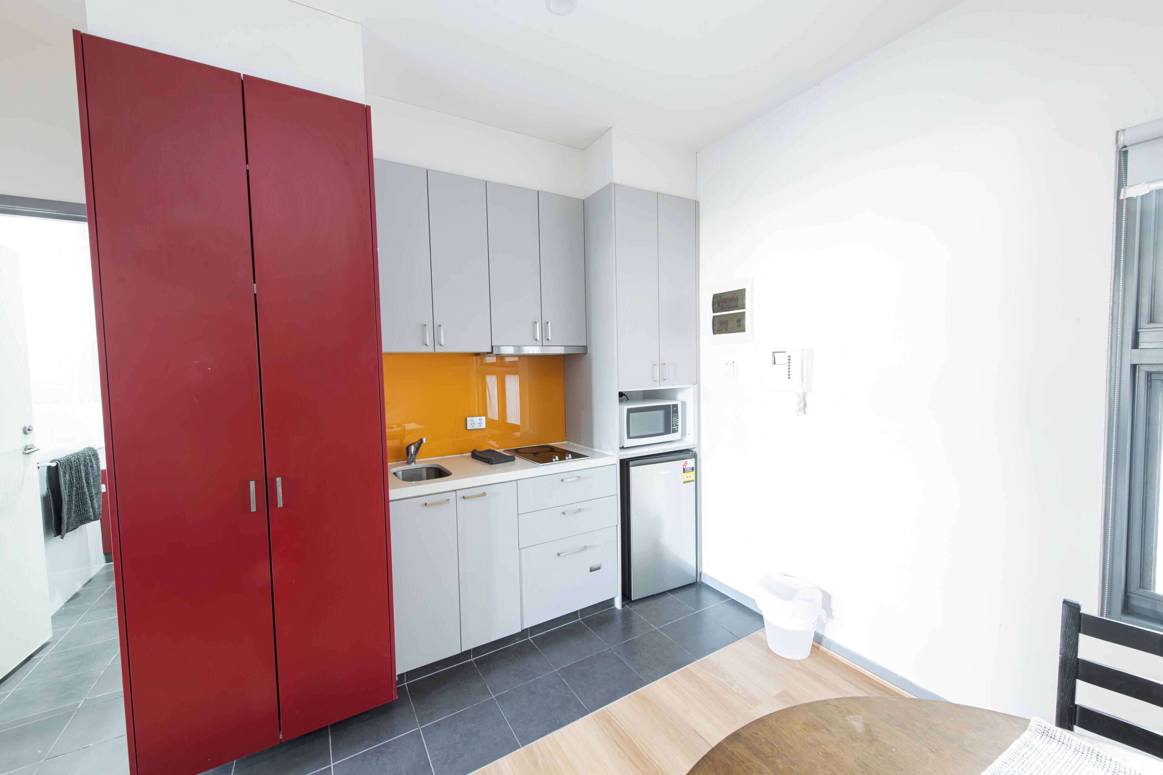 Een moderne keuken met grijze kastjes, een rode garderobe en een magnetron.