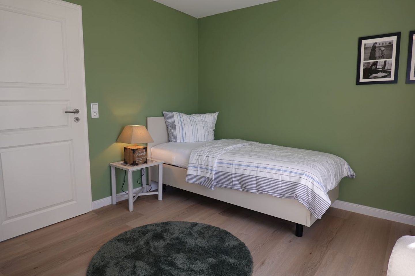Une chambre à coucher avec un lit, une table de chevet avec une lampe, un mur vert et une porte.