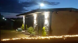 A small, single-story building with a stone facade and a flat roof, illuminated by exterior lights. - 1bed Cottage, Sleeps 2 - Mountain Views, Parking (Neath)
