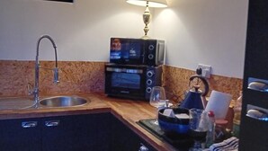 A compact kitchen with a sink, a microwave, a toaster, and a table with a glass and a bottle. - 1bed Cottage, Sleeps 2 - Mountain Views, Parking (Neath)