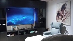 A modern living room with a large flat-screen TV, a grey armchair, and a mounted painting of a horse. - 1bed Cottage, Sleeps 2 - Mountain Views, Parking (Neath)