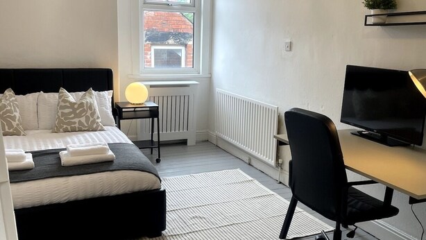 Un dormitorio moderno con cama, mesita de noche, lámpara y un escritorio con ordenador.