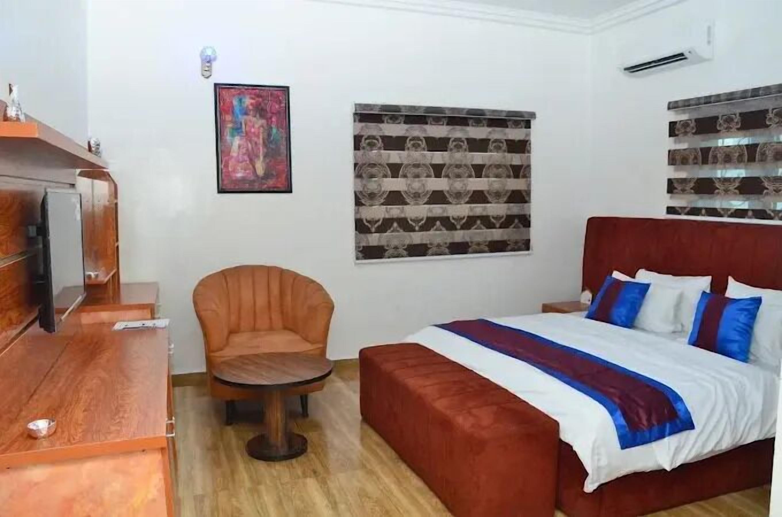 Un dormitorio con un escritorio de madera, un sillón de cuero, una cama con cabecera roja y un adorno de pared con estampado.