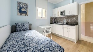 Ein kleines Schlafzimmer mit Bett, einer kompakten Küchenzeile und einem Fenster.