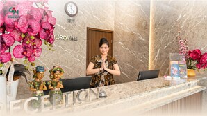 Un comptoir de réception d’hôtel avec un revêtement en marbre, une horloge et des orchidées décoratives.