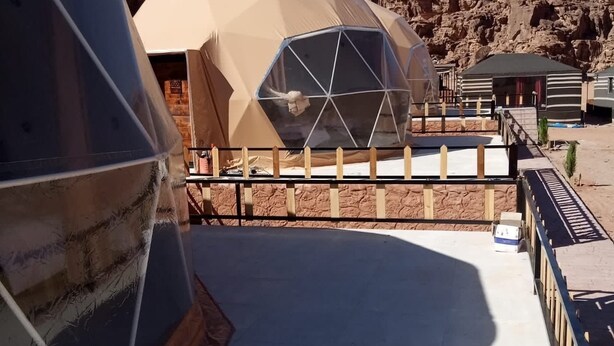 A desert resort with geodesic dome accommodations, a paved walkway, and rocky cliffs in the background. - Wadi Rum Desert Camp (Wadi Rum)
