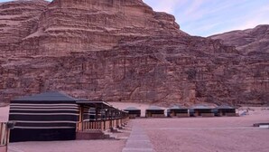 A desert resort with a row of cabins and a large tented area. - Wadi Rum Desert Camp (Wadi Rum)