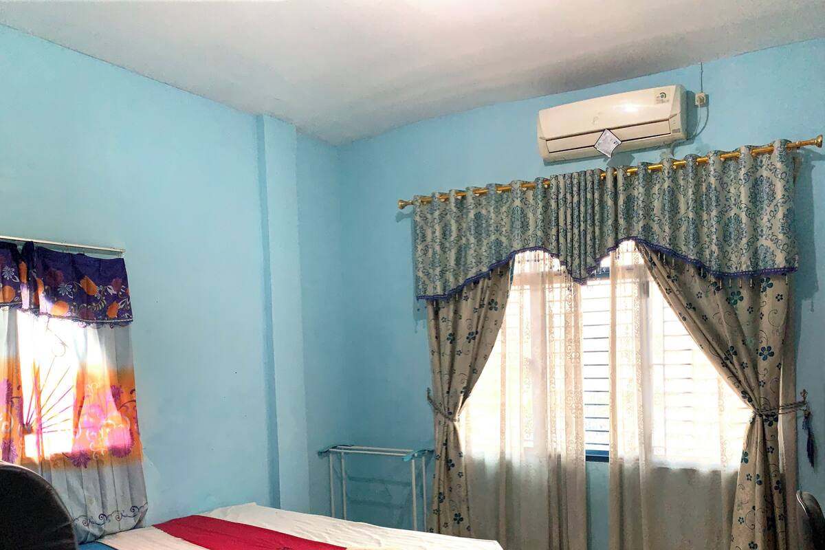 Una camera da letto con un letto, una finestra con tende, un condizionatore d'aria e un termosifone.