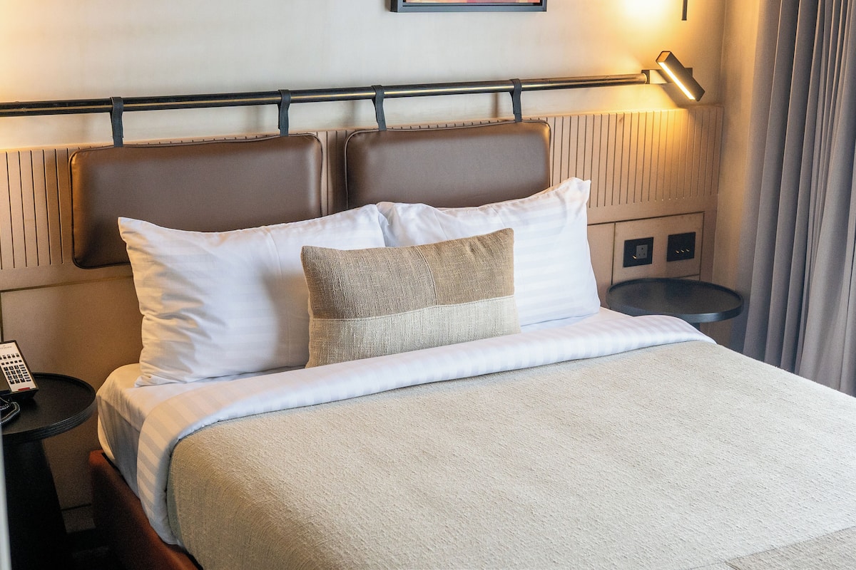 Une chambre d’hôtel avec un lit, une table de chevet avec un téléphone et une lampe fixée au mur.