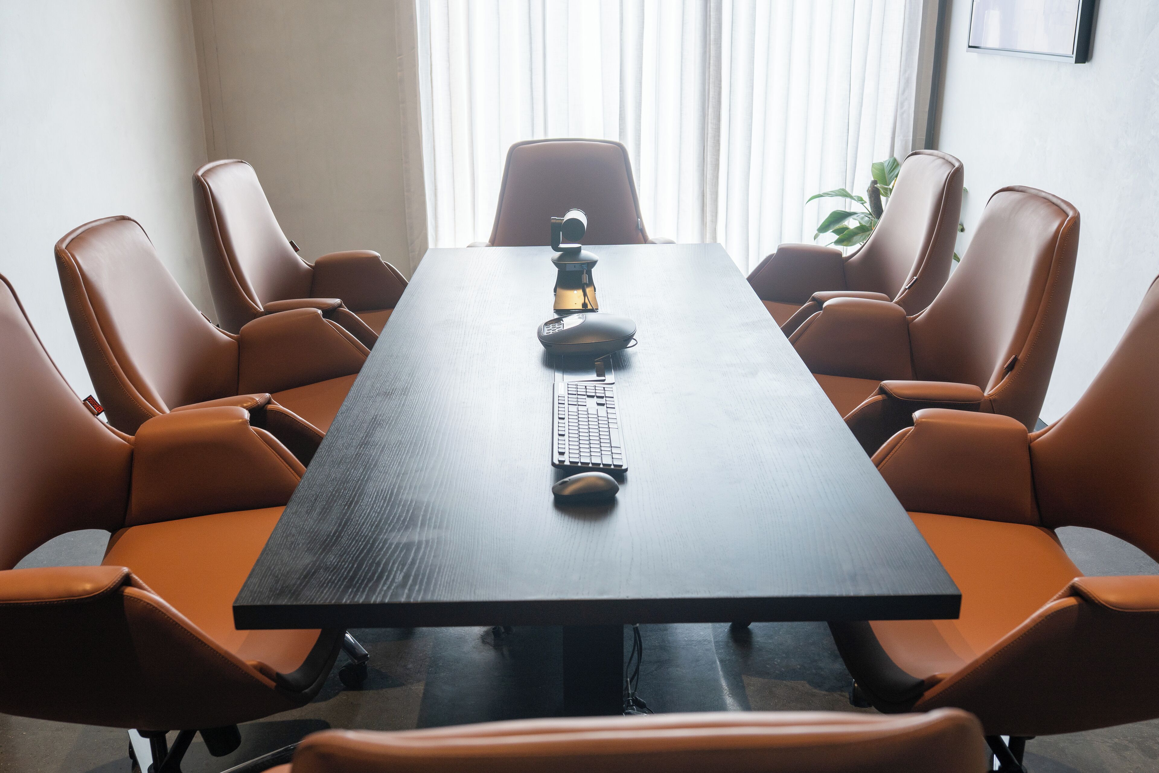 Une salle de conférence avec une longue table, six chaises en cuir marron, un clavier et une souris posés sur la table.