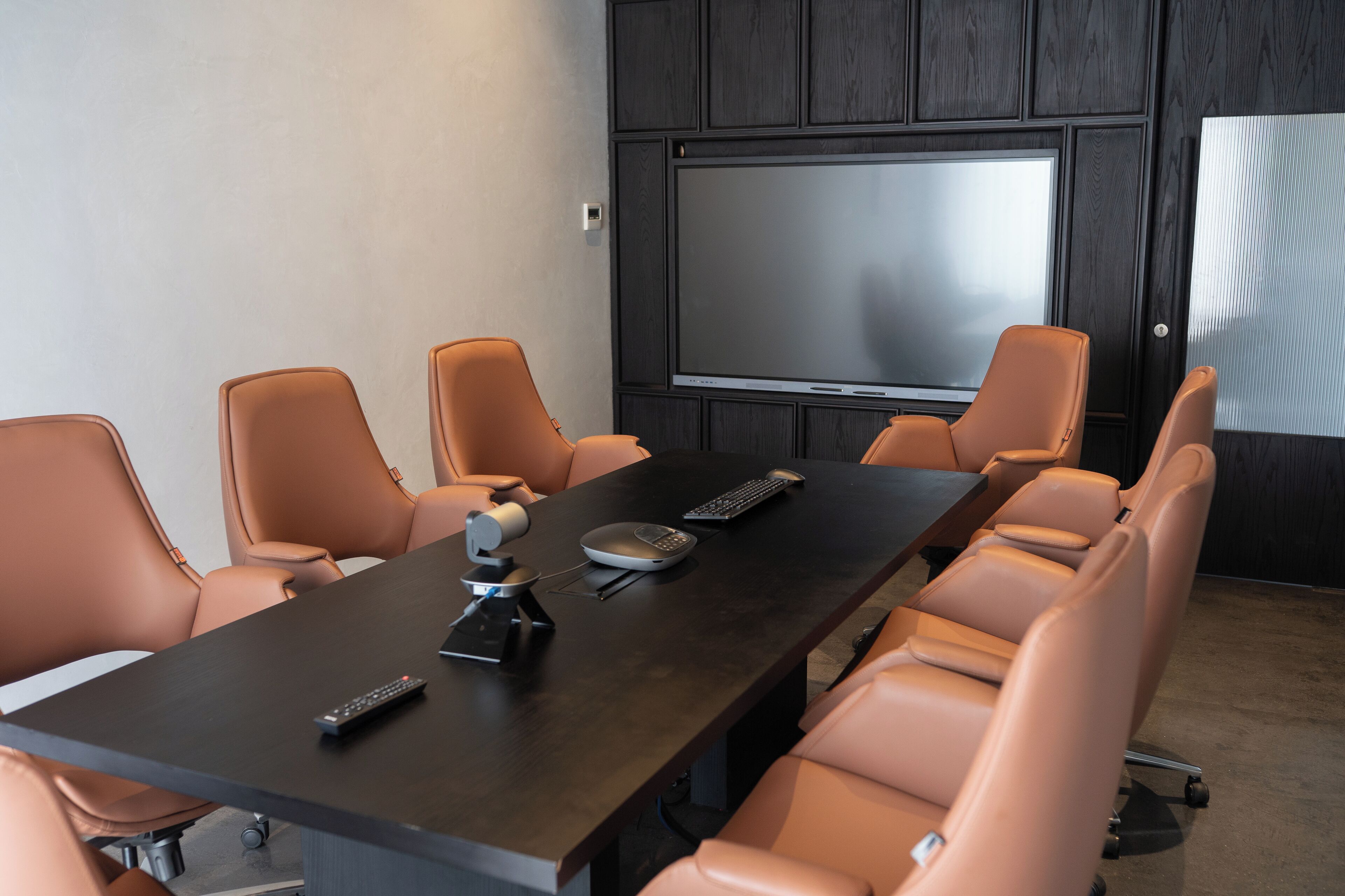 A conference room with a dark wooden table, six leather chairs, a large screen, and a projector.