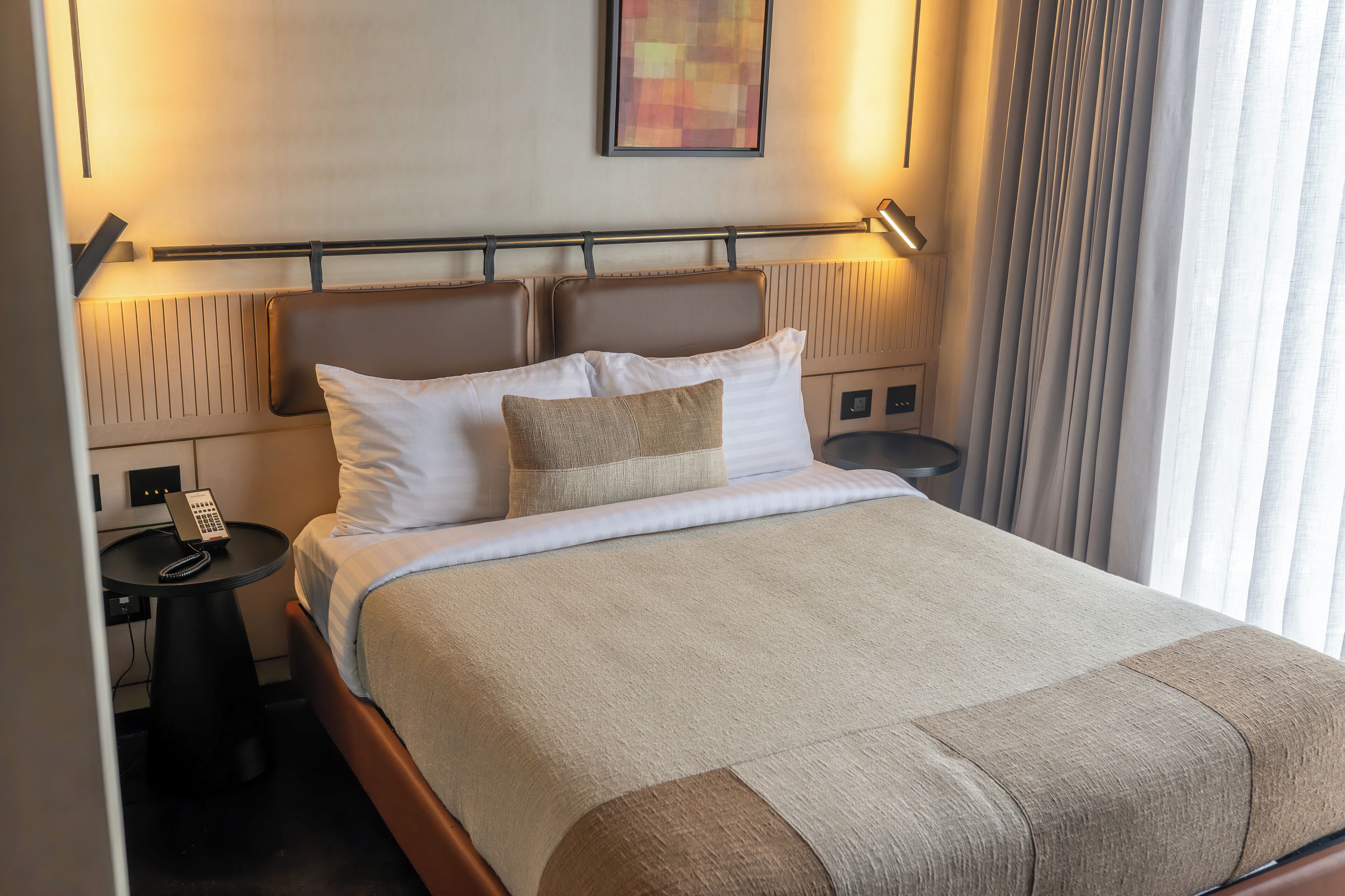 Una habitación de hotel con cama, mesitas de noche, teléfono y lámpara.