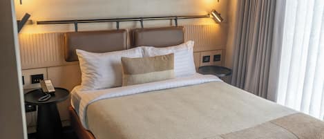 Una habitación de hotel con cama, mesitas de noche, teléfono y lámpara.