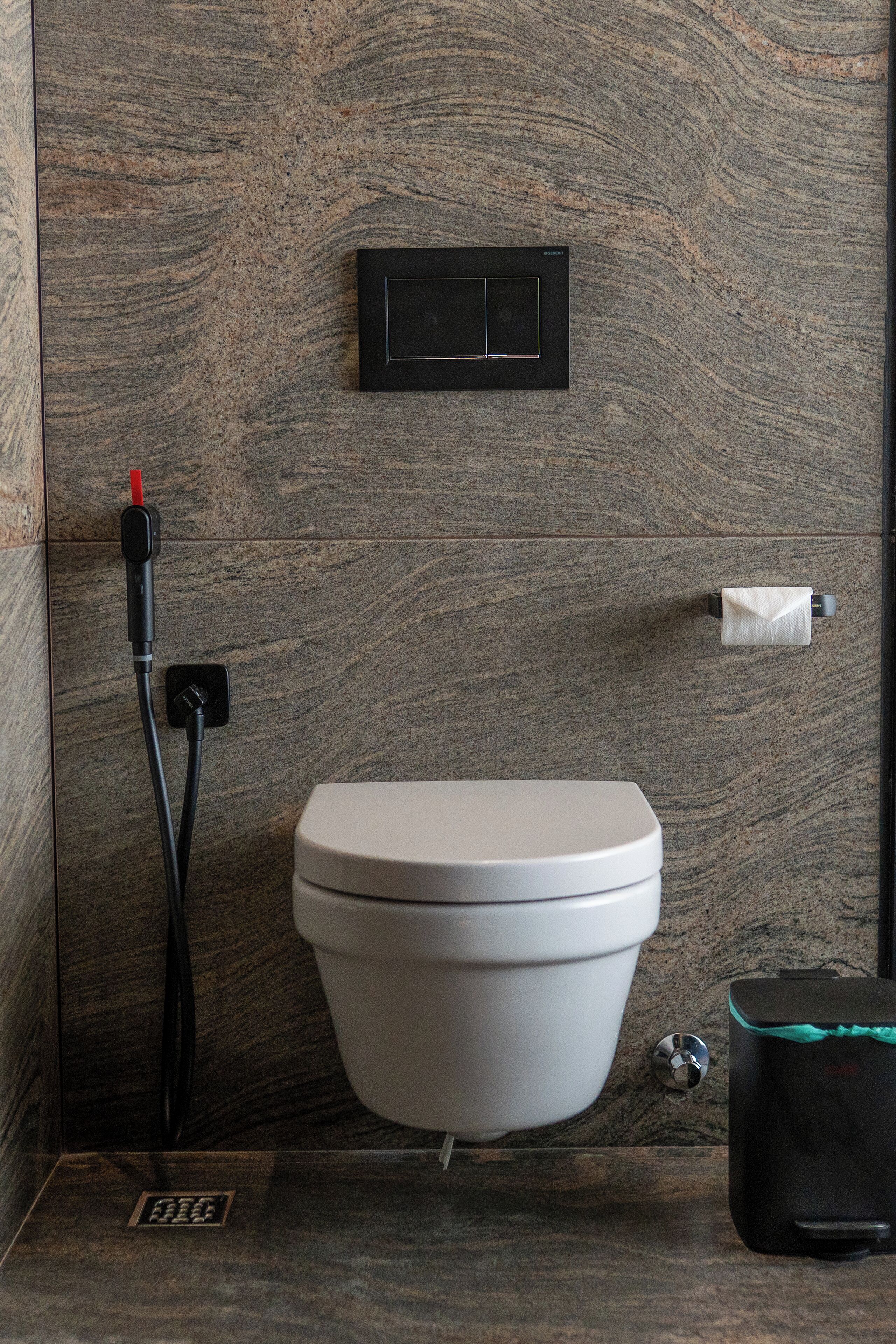 A modern bathroom with a toilet, a paper towel dispenser, and a black electrical outlet.